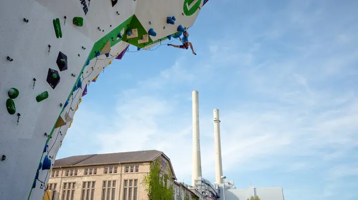 © Im Vordergrund Kletterer beim Seilklettern am Kletterturm im Außenbereich, im Hintergrund Kletterhalle