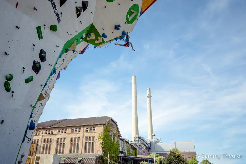 © Im Vordergrund Kletterer beim Seilklettern am Kletterturm im Außenbereich, im Hintergrund Kletterhalle
