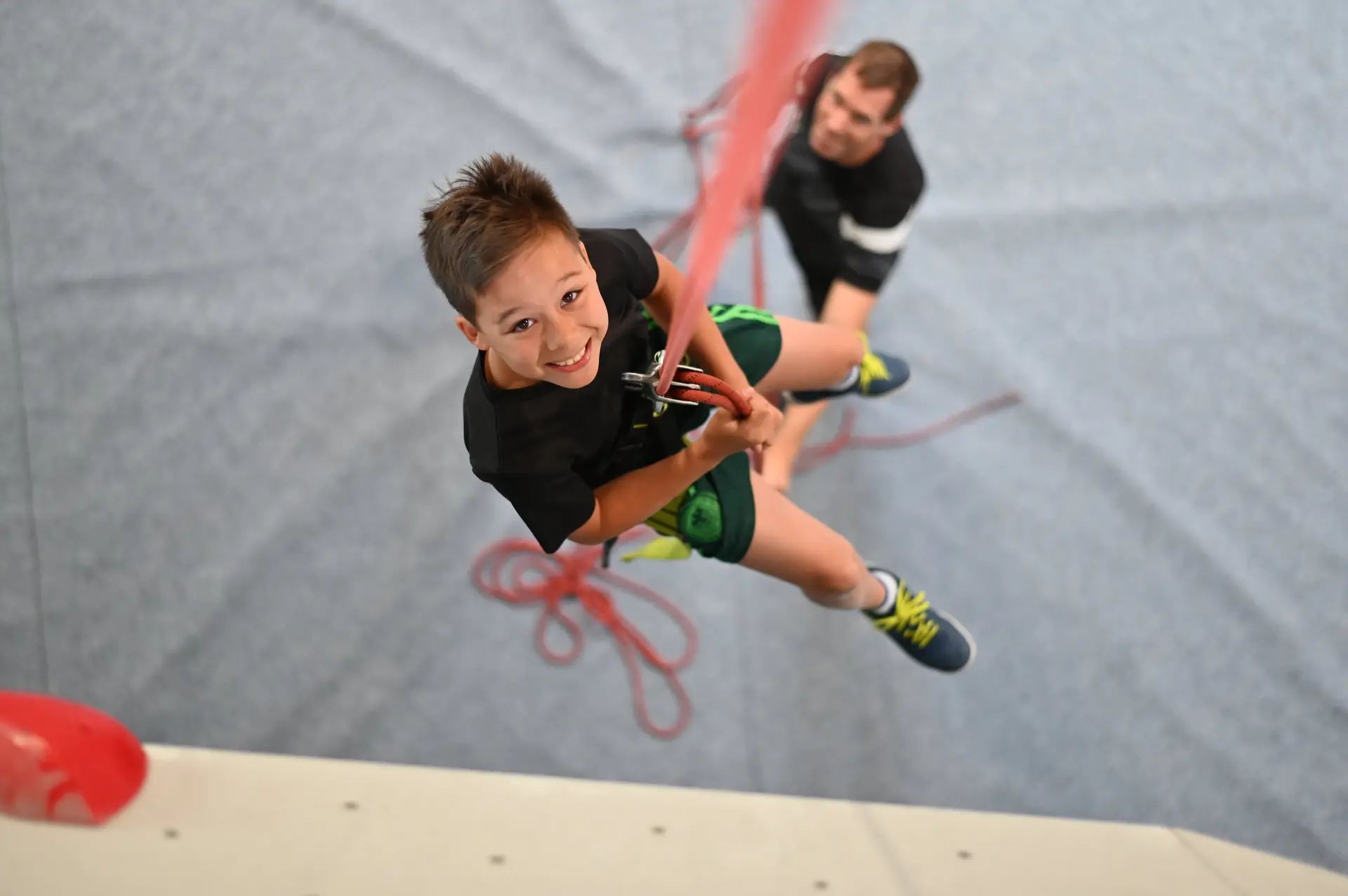 Kind hängt am Seil an der Kletterwand und lächelt | © diekletterarena