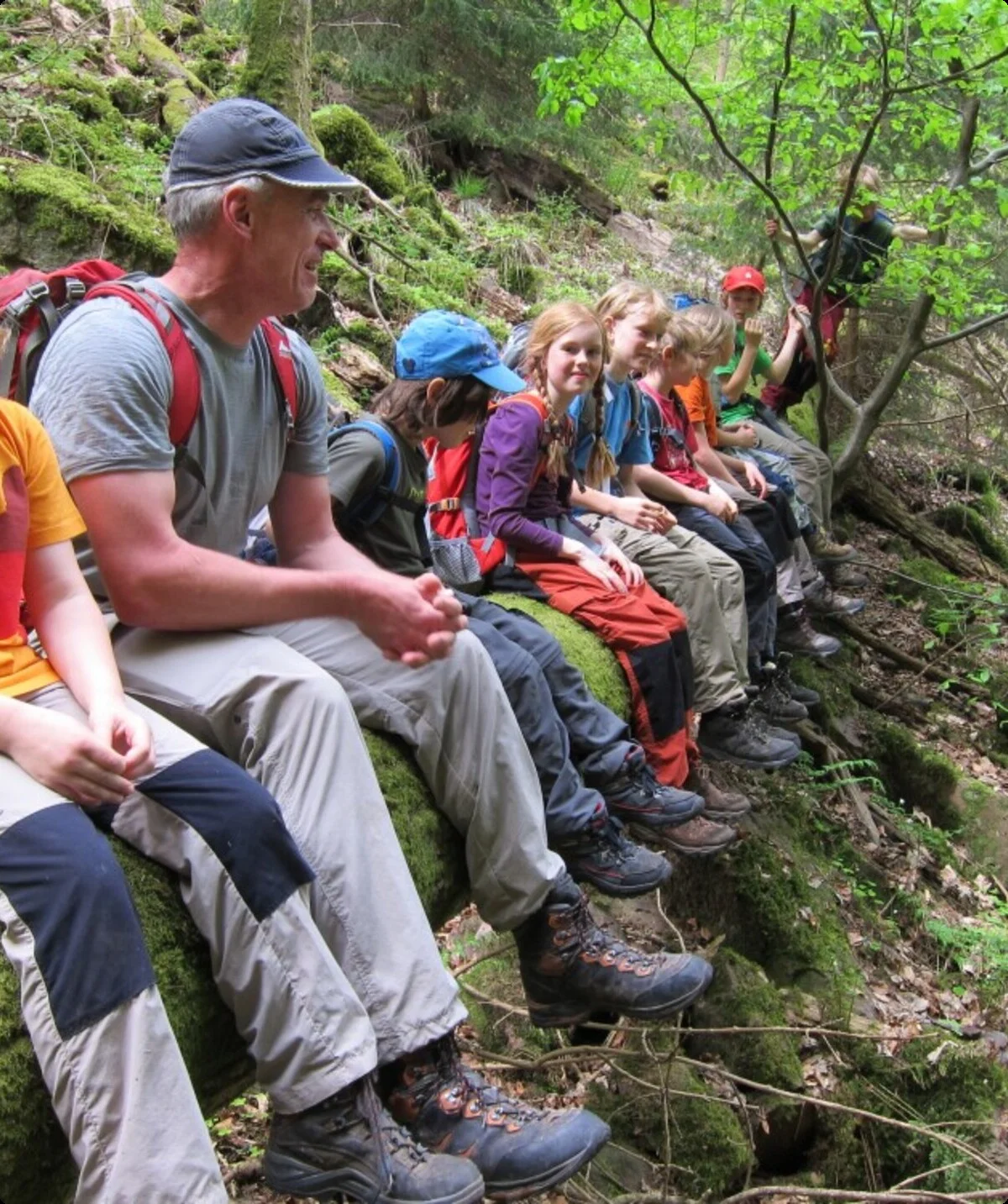 zahlreiche Kinder und ein Mann sitzen auf einem umgestürzten Baumstamm und lachen in die Kamera | © DAV Heilbronn