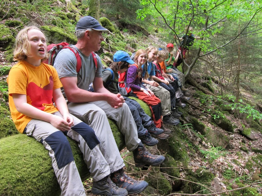 zahlreiche Kinder und ein Mann sitzen auf einem umgestürzten Baumstamm und lachen in die Kamera | © DAV Heilbronn