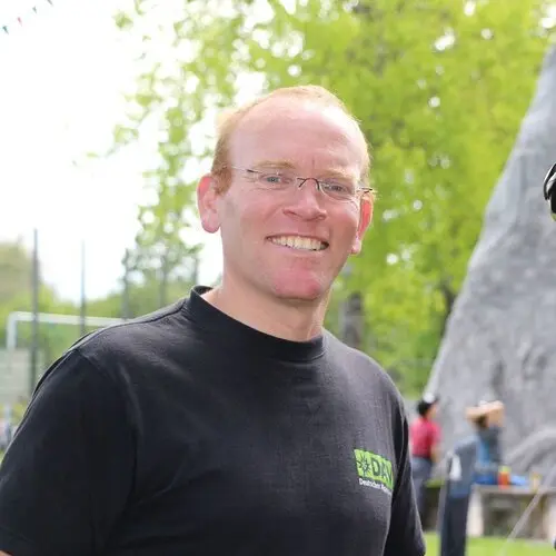 lächelnder Mann mit Brille und kurzen roten Haaren in einem schwarzen T-Shirt | © DAVhn