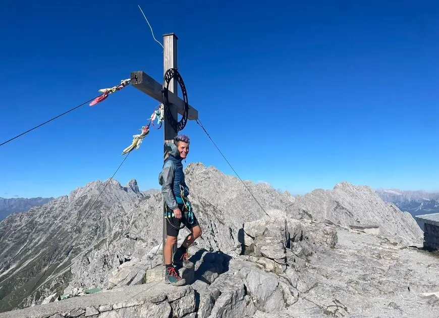 lachende Frau an einem Gipfelkreuz mit kurzen, hellen Haaren | © DAV Heilbronn