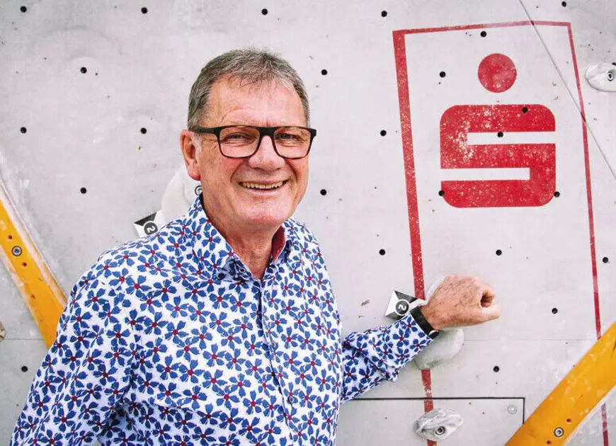 lachender Herr mit Brille und einem blau-weißen Hemd mit Blütenmuster vor einer Kletterwand | © DAV Heilbronn