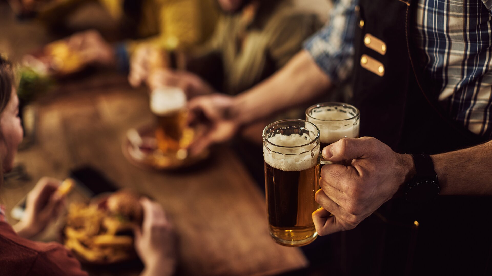 Kellner bringt zwei volle Bierkrüge an Tisch mit zwei Personen. Im Hintergrund sieht man diese Personen verschwommen. | © freepik