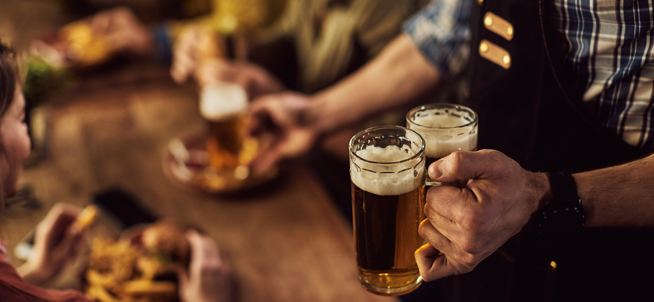 Kellner bringt zwei volle Bierkrüge an Tisch mit zwei Personen. Im Hintergrund sieht man diese Personen verschwommen. | © freepik