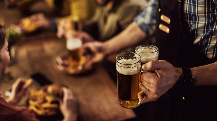 Kellner bringt zwei volle Bierkrüge an Tisch mit zwei Personen. Im Hintergrund sieht man diese Personen verschwommen. | © freepik
