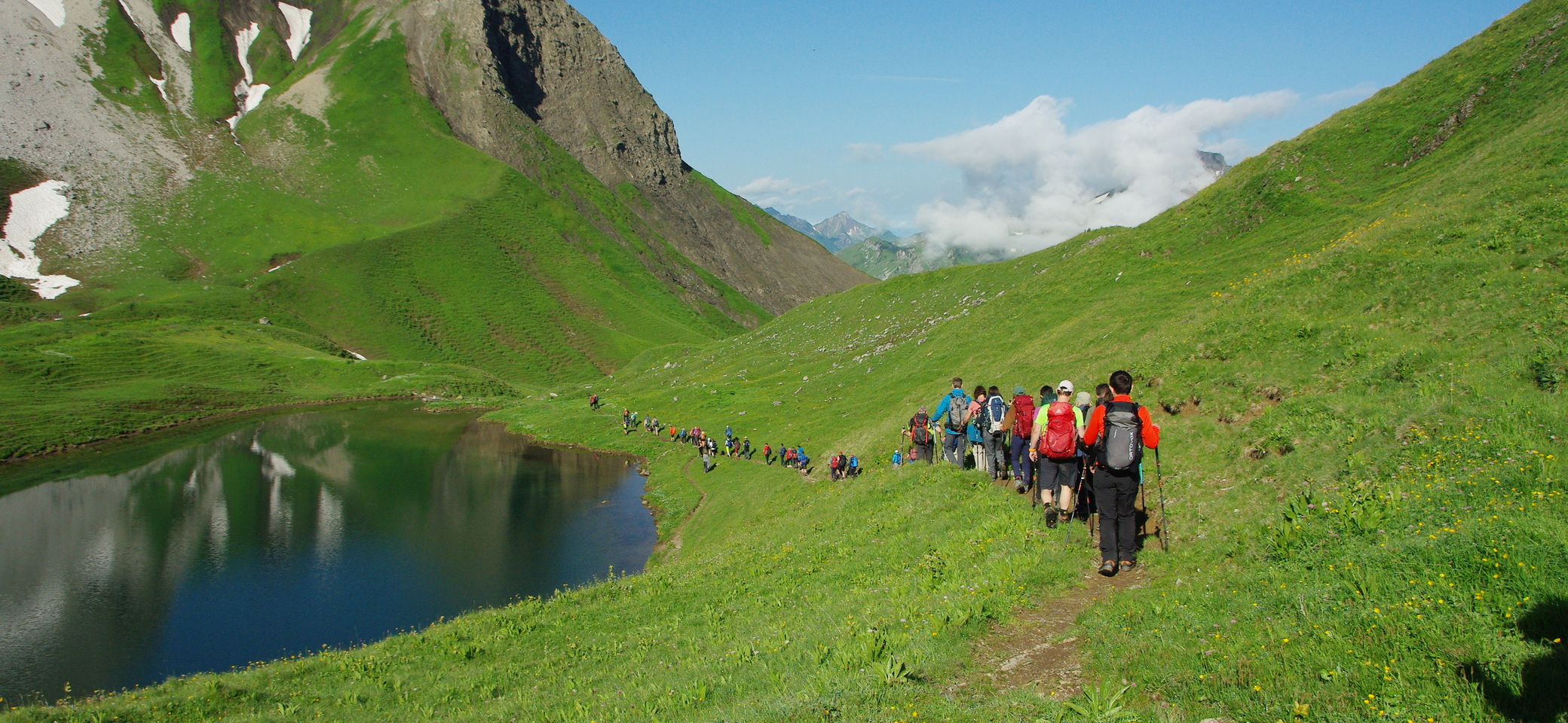Viele Menschen wandern hintereinander an einem See vorbei. Sie sind von Bergen umgeben | © DAV Heilbronn