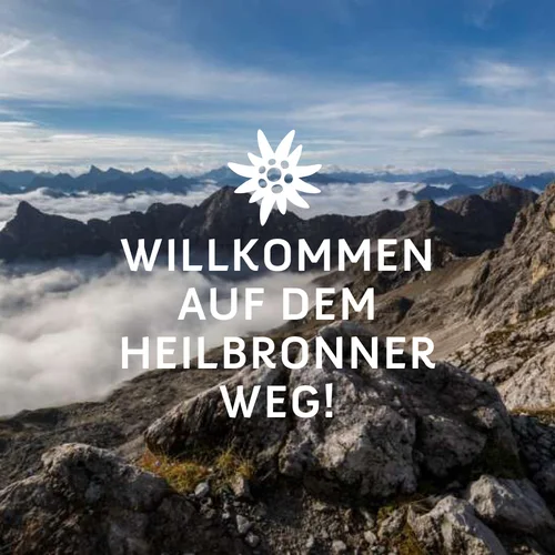 Willkommen auf dem Heilbronner Weg. Weiße Schrift mit weißem Edelweiß. Im Hintergrund Berge im Nebel. | © DAV Sektion Heilbronn DAV Sektion Heilbronn | © DAV Sektion Heilbronn